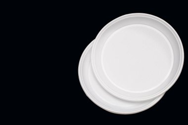 Disposable white plastic plates on a black background. Free space for text. Disposable plastic tableware for picnic or outdoor party. Plastic pollution and environmental problems