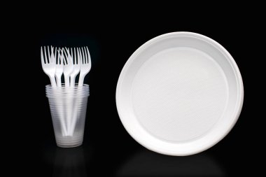 Disposable white plastic tableware in the form of plates, glasses and forks on a black background. Plastic utensils for a picnic or outdoor party. Plastic pollution and environmental issues
