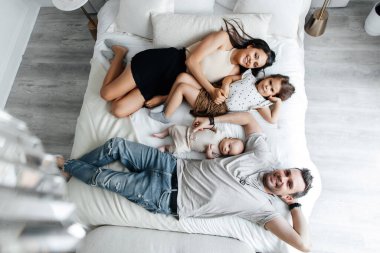Young parents and their children lie in bed top view. Father, mother and their daughter and newborn son spend the day off at home and have fun in bed. Happy family enjoy spending time with each other