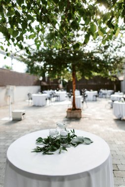 Tables for guests decorated with floating candles and green leaves. Preparing for an outdoor party with beautiful candle and leaf decor. Party in a beautiful place with trees
