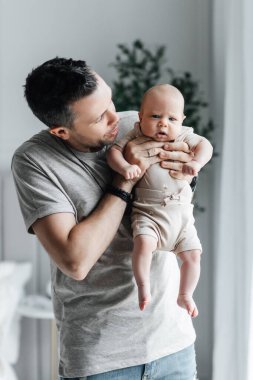 Loving dad holds his newborn baby in his arms. Stylish father and his cute newborn son. Parental relationship between father and son. Happy fatherhood and the joy of being a father