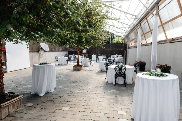 The restaurant is in a beautiful location with decorated tables and trees in the center. Preparation for the reception of guests and table setting. Restaurant with transparent roof and beautiful decor