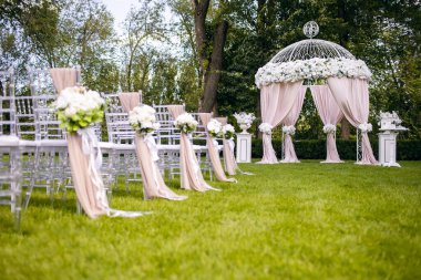 Güzel bir düğün kemeri ve yeşil çimlerde beyaz sandalyeler. Düğün merasimine hazırlanıyorum. Düğün kemeri ve konuklar için sandalyeler beyaz çiçeklerle süslenmiş.