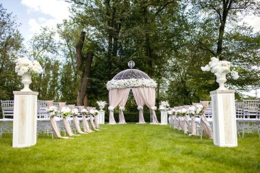 Düğün töreni için yeşil çimenlikte güzel düğün kemeri ve beyaz sandalyeler. Yeni evlilerin düğün kemeri ve konuklar için sandalyeler beyaz çiçeklerle süslenmiş.