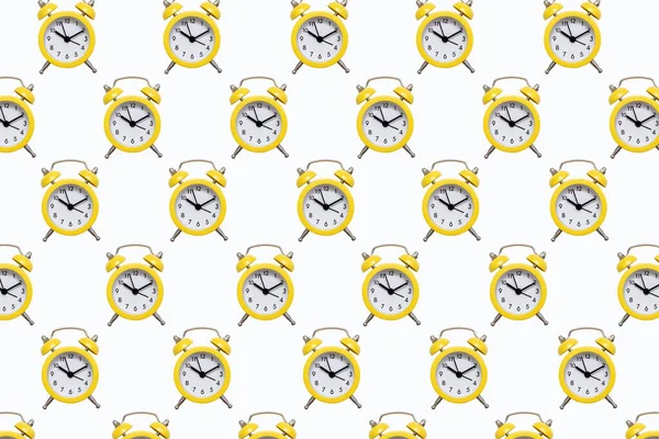 Pattern from yellow alarm clocks on a white isolated background. The background of many small alarm clocks in the form of a pattern. The concept of punctuality in the form of bright alarm clocks
