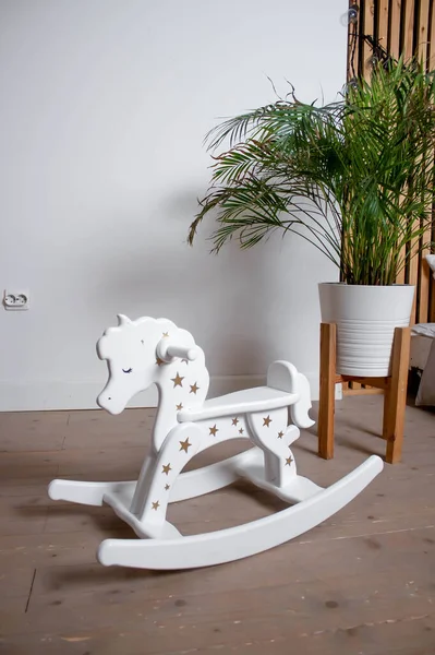 Children\'s rocking horse with stars. A flower on the floor. Against the background of a white wall.