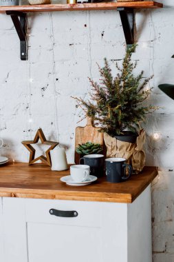 Mutfak setindeki bir tencerede küçük bir Noel ağacı. Bardaklar, fincan ve çay tabağı masanın üstünde..