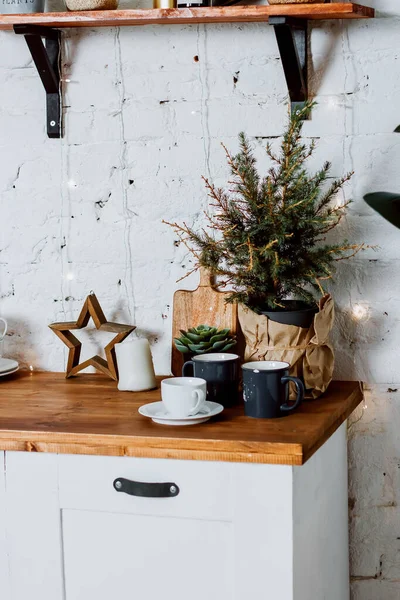 Mutfak setindeki bir tencerede küçük bir Noel ağacı. Bardaklar, fincan ve çay tabağı masanın üstünde..