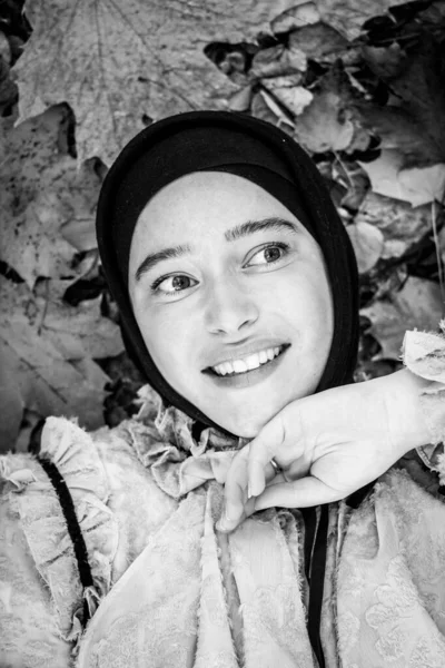 カラフルな紅葉の背景にヒジャーブのイスラム教徒の女性 美人写真 ピンクのブラウス 笑顔だ 秋の紅葉 顔をクローズアップ 白黒写真 — ストック写真