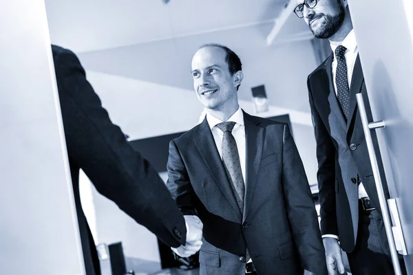 Grupp av självsäkra affärsmän hälsning med ett handslag på affärsmöte i moderna kontor eller avsluta affären avtalet genom att skaka hand. — Stockfoto