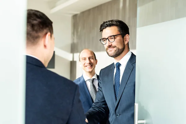 Groep van vrolijke zelfverzekerde zakenmensen begroeten met een handdruk op zakelijke bijeenkomst in modern kantoor. — Stockfoto