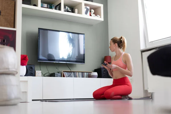 Atrakcyjna sportowa kobieta ćwicząca w domu, ćwicząca pilates przed telewizorem w swoim małym mieszkaniu. Odległość społeczna. — Zdjęcie stockowe