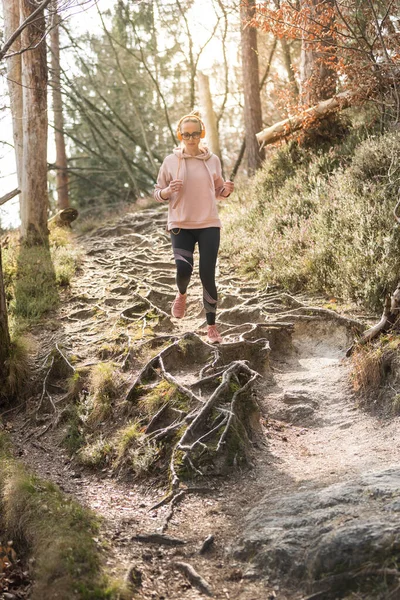 Active sporty woman listening to the music while running in autumn fall forest. Female runner training outdoor. Healthy lifestyle image of young caucasian woman jogging outside — Stock Photo, Image