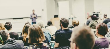 Üniversitedeki konferans salonunda sunum yapan adam.