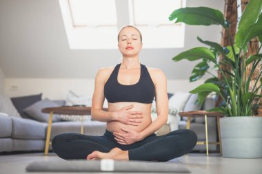 Genç, güzel, hamile bir kadın yoga yapıyor, karnını okşuyor. Genç, mutlu, rahatlatıcı, bebeğini düşünüyor ve gelecekteki hayatından zevk alıyor. Annelik, hamilelik, yoga konsepti.