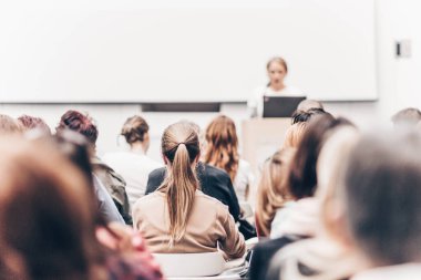 İş ve girişimcilik sempozyumu. İş toplantısında kadın konuşmacı bir konuşma yapıyor. Konferans salonunda dinleyiciler. İzleyicilerin tanınmayan katılımcılarının arka görünümü.