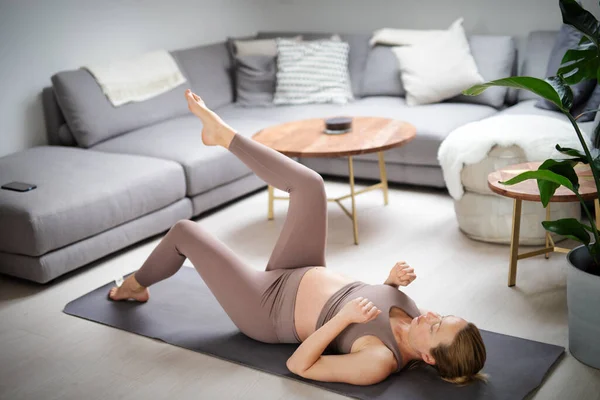 Młoda piękna ciężarna kobieta trenuje pilates w domu w swoim salonie. Zdrowy styl życia i aktywna koncepcja ciąży i macierzyństwa. — Zdjęcie stockowe