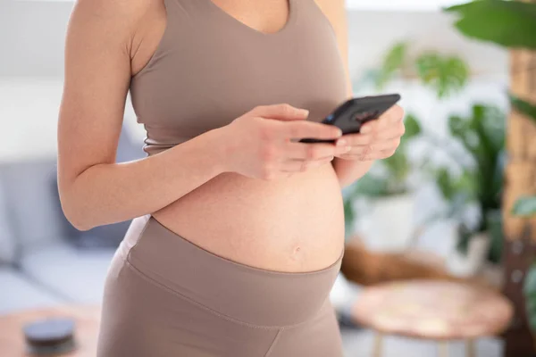 孕妇腹部的特写照片。在家中持用手机的妇女。怀孕、技术、网上购物、准备和期望概念. — 图库照片