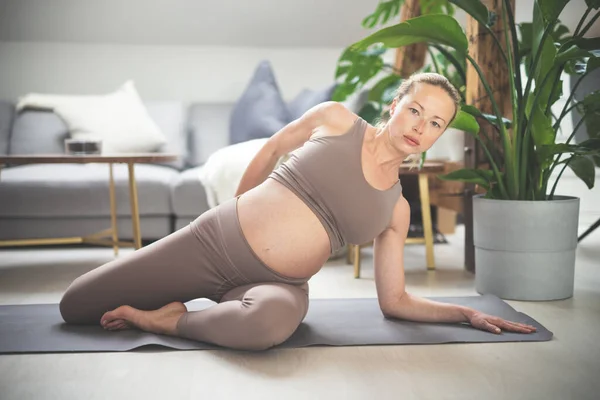 Jonge mooie zwangere vrouw traint pilates thuis in haar woonkamer. Gezond leven en actief zwangerschaps- en moederschapsconcept. — Stockfoto