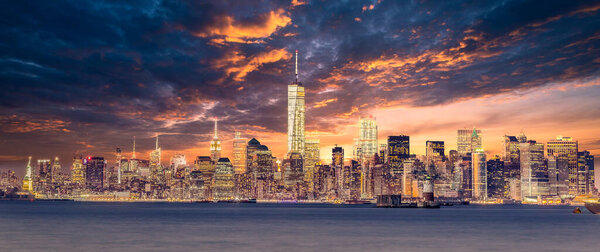 New York City Manhattan downtown skyline at dusk with skyscrapers illuminated over Hudson River panorama. Dramatic sunset sky.