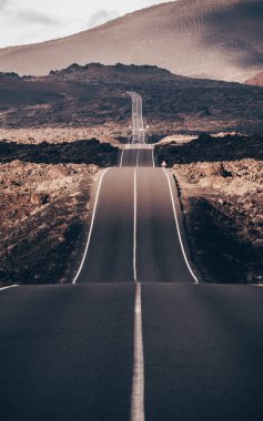Kanarya Adaları 'ndaki Lanzarote' deki Timanfaya Ulusal Parkı 'nda sonsuz bir yol. Aralıksız bir çizgi, siyah volkanik kayalar ve arka planda sisli volkanlar..