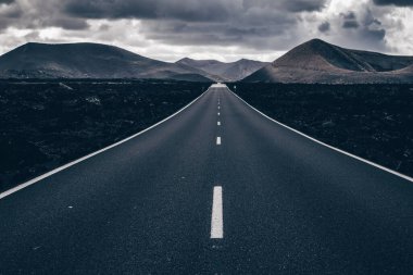 Kanarya Adaları 'ndaki Lanzarote' deki Timanfaya Ulusal Parkı 'nda sonsuz bir yol. Aralıksız bir çizgi, siyah volkanik kayalar ve arka planda sisli volkanlar..