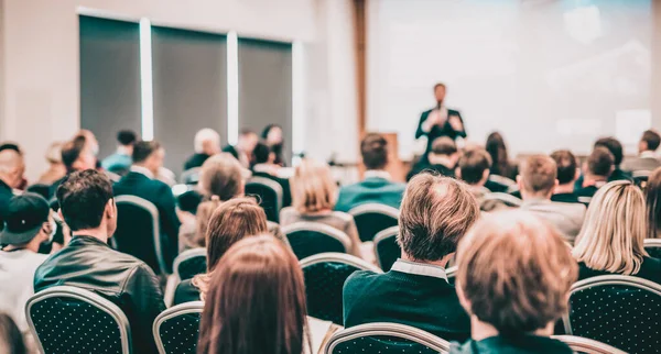 Redner hält einen Vortrag im Konferenzsaal bei einer Veranstaltung. Rückansicht unkenntlich gemachter Personen im Publikum des Konferenzsaals. Unternehmens- und Unternehmerkonzept. — Stockfoto