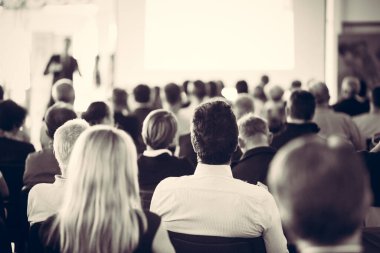 İş toplantısında konferans salonunda konuşma yapan konuşmacı. Konferans salonundaki tanınmayan seyircilerin arka görüntüsü.