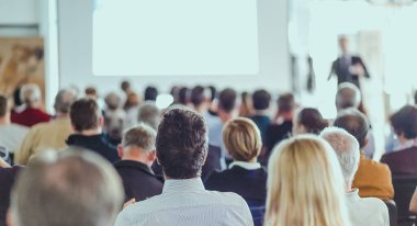 İş toplantısında konferans salonunda konuşma yapan konuşmacı. Konferans salonundaki tanınmayan seyircilerin arka görüntüsü.