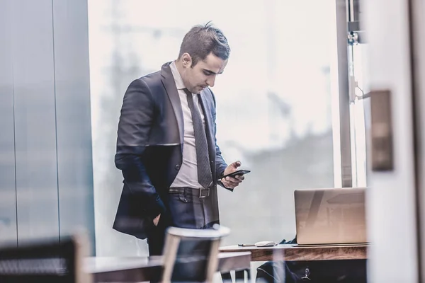 Бизнесмен смотрит на смартфон в современном корпоративном офисе . — стоковое фото