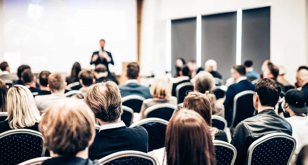 Redner hält einen Vortrag im Konferenzsaal bei einer Veranstaltung. Rückansicht unkenntlich gemachter Personen im Publikum des Konferenzsaals. Unternehmens- und Unternehmerkonzept. — Stockfoto