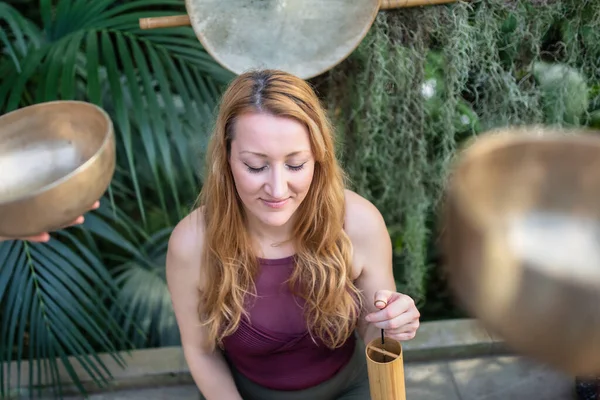 Yoga koncept, meditation och ljudterapi. Vacker ung kaukasiska kvinna omgiven av koppar tibetanska sjungande skålar och instrument. — Stockfoto