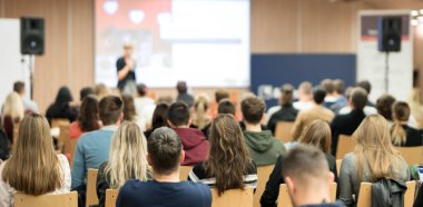 İş ve girişimcilik sempozyumu. İş toplantısında kadın konuşmacı bir konuşma yapıyor. Konferans salonunda dinleyiciler. İzleyicilerin tanınmayan katılımcılarının arka görünümü.