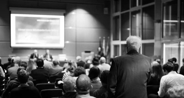 I have a question. Group of business people sitting at the chairs in conference hall. Businessman raising his arm. Conference and Presentation. Business and Entrepreneurship.