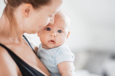 Annesinin kollarında dinlenen, kameraya bakan tatlı bir bebeğin portresi. Yeni anne kucağında ve kucağında küçük bir çocuk, şefkatle, sevgiyle, özenle çocuğunu kucaklıyor. Annelik kavramı.