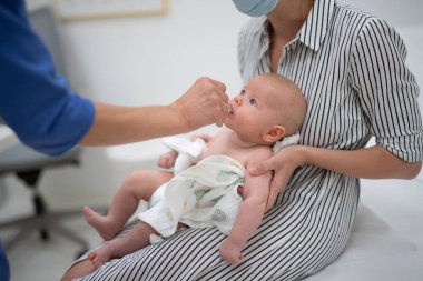 Pediyatrist annesinin huzurunda küçük bebeğe rotavirüs enfeksiyonuna karşı ağız aşısı yapıyor. Çocuk sağlığı ve hastalık önleme.