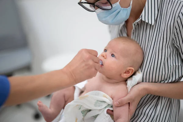 小児科医は 母親の前で小さな赤ちゃんへのロタウイルス感染に対する経口予防接種を管理しています 子どもの健康管理と疾病予防 ロイヤリティフリーのストック画像