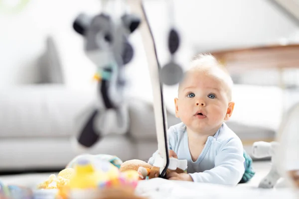 自宅でマットの上に吊るされたおもちゃのアーチで遊ぶかわいい赤ちゃんの男の子赤ちゃんの活動と幼児発達のための遊び場 家で遊んでる赤ちゃん ロイヤリティフリーのストック画像