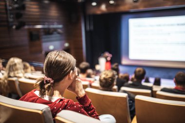 İş ve girişimcilik sempozyumu. İş toplantısında kadın konuşmacı bir konuşma yapıyor. Konferans salonunda dinleyiciler. İzleyicilerin tanınmayan katılımcılarının arka görünümü.