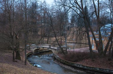 Nehir ve şehir parkındaki eski güzel taş köprü Sonbaharda büyük yaşlı ağaçlarla