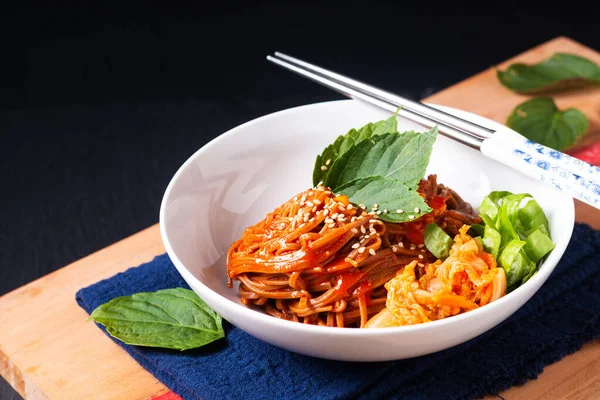 Food concept korean spicy cold buckwheat noodle Kimchi Bibim Guksu on wooden board and black background with copy space