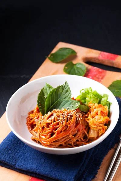 Food concept korean spicy cold buckwheat noodle Kimchi Bibim Guksu on wooden board and black background with copy space