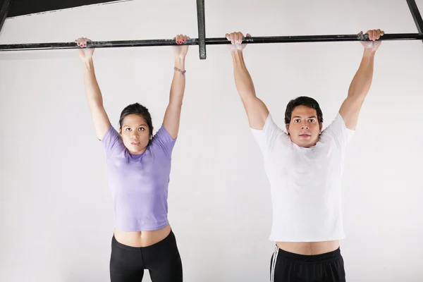 Kvinnliga och manliga kroppsbyggare gör pull-ups på metall bomma till på gymmet — Stockfoto