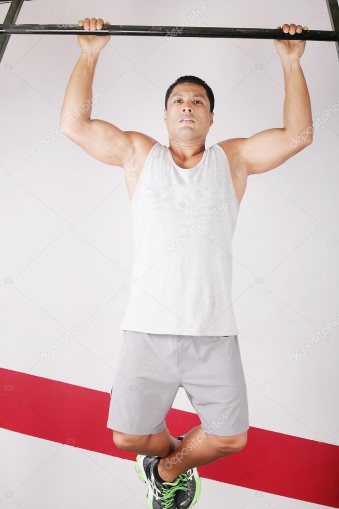 Strong man doing pull ups on a bar in a gym in the background.