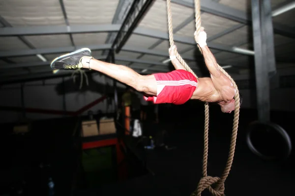 Crossfit cuerda subir entrenamiento sobre un fondo oscuro . — Foto de Stock