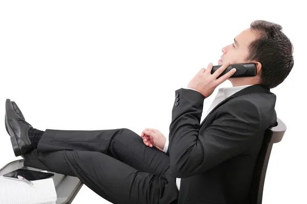 Young business man relaxing at office desk and talking on mobile — Stock Photo, Image