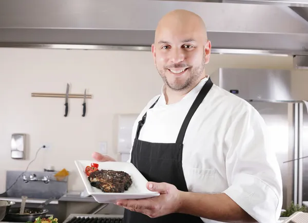 Young male chef presenting a juicy ribeye steak with tomatoes — Stock Photo, Image