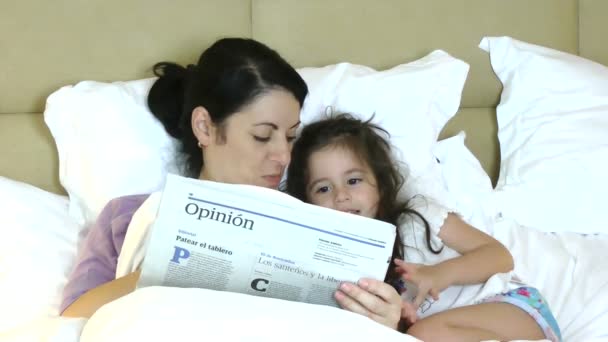 Mother and child reading newspaper in bed having fun — Stock Video