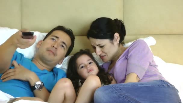 Familie liegt im Bett vor dem Fernseher und benutzt eine Fernbedienung — Stockvideo