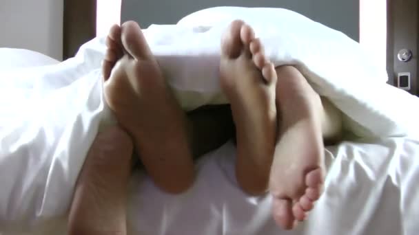 Loving couple in bed at home. Close-up of human legs stretching out of the blanket in bedroom. — Stock Video